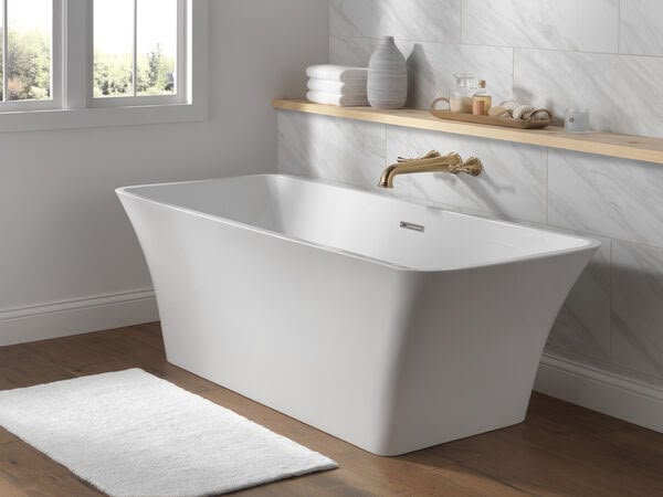 Freestanding tub with wall mount faucet in brushed gold finish, against marble wall
