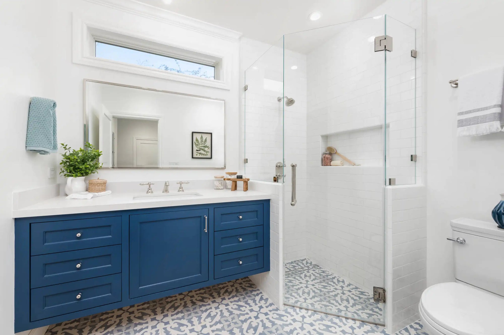 A modern bathroom with blue vanity cabinets, patterned tile flooring, and glass corner shower stalls. |ACE DECOR