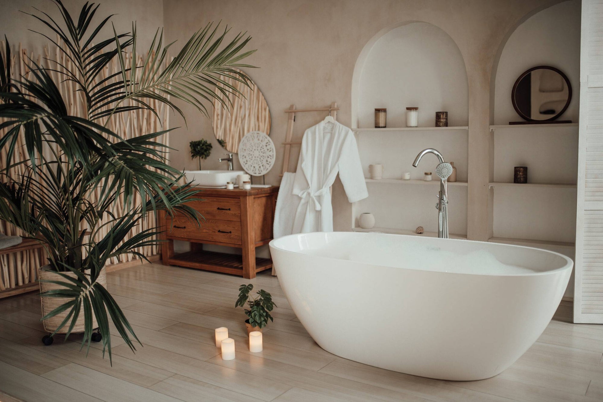 A warm, spa-inspired bathroom retreat with a stone resin bathtub surrounded by natural wood elements, greenery, and soft candlelight. | ACE DECOR