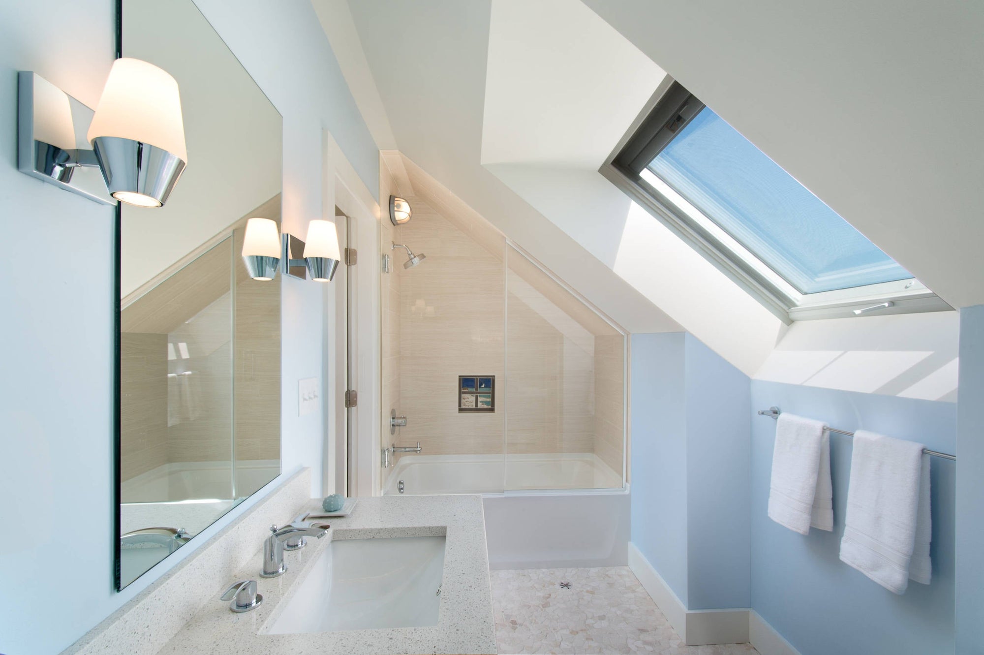 A modern attic bathroom featuring a sleek bathtub with a clear glass shower door, under a large skylight that fills the space with natural light. | ACE DECOR