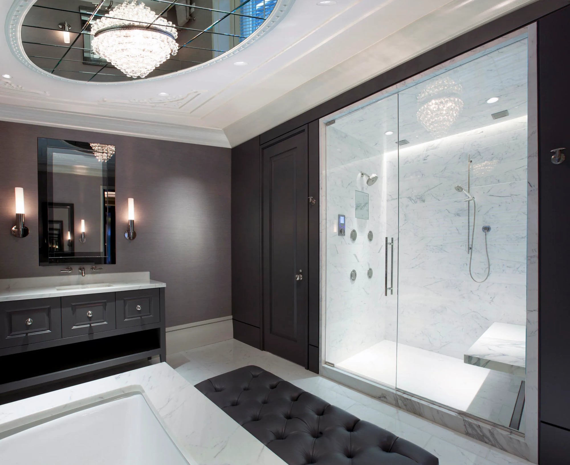 Luxurious modern bathroom with dark gray walls, black vanity and mirror with wall sconces, frameless glass shower enclosure with multiple jets, white marble floor, black tufted bench