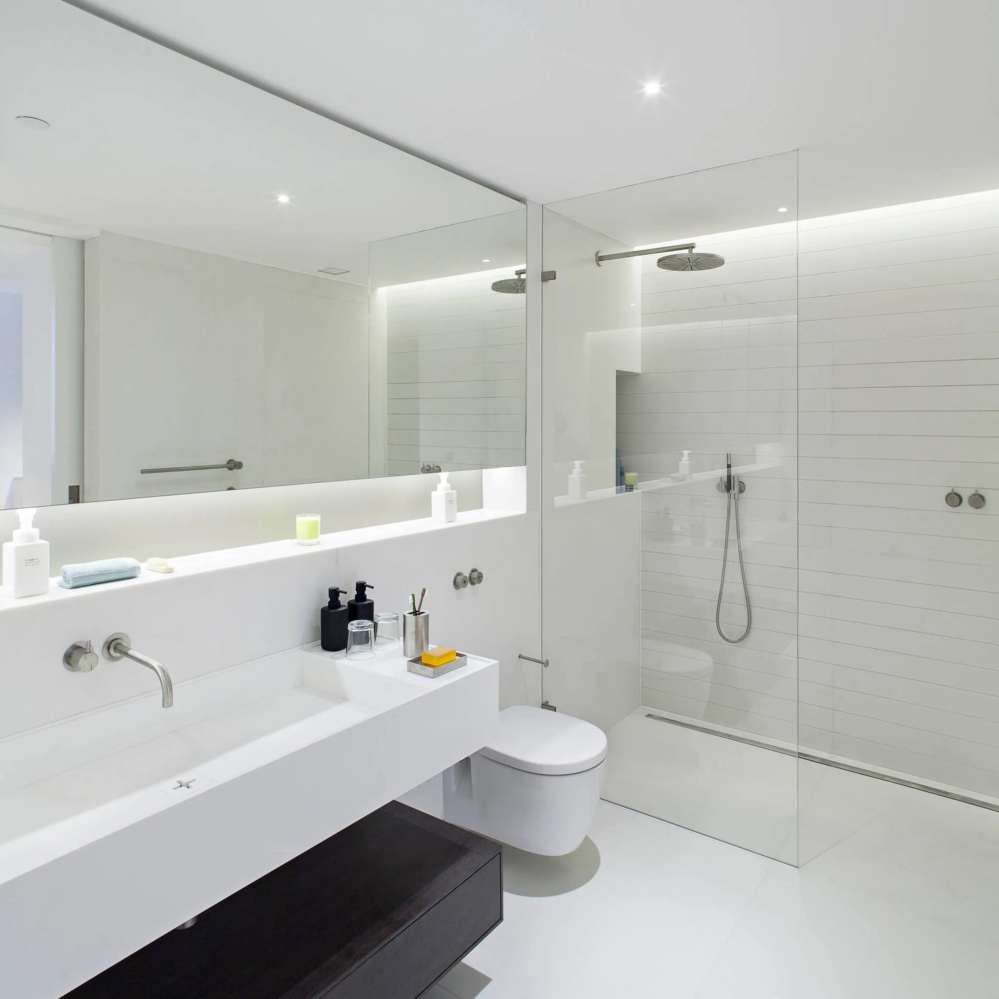 Modern white bathroom with glass shower enclosure featuring sleek shower head, minimalist design with clean lines and large mirror.