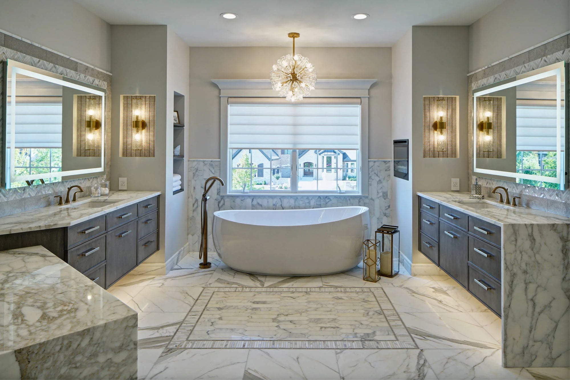 Elegant spa-inspired bathroom with a freestanding white tub, antique-style faucet, dual marble vanities, and gold-leaf accents under a crystal chandelier.