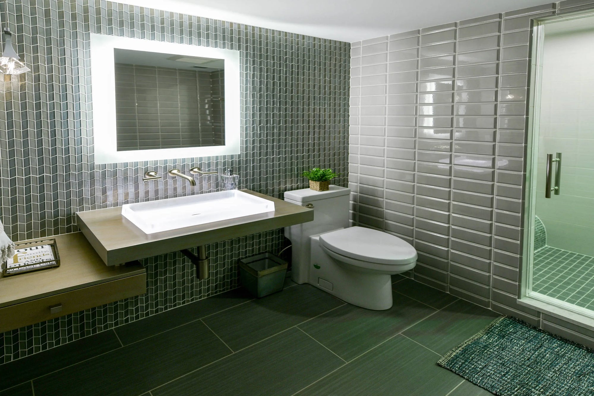 Modern basement bathroom with green tile walls, illuminated mirror, and toilet featuring a compact basement upflush system for efficient plumbing.