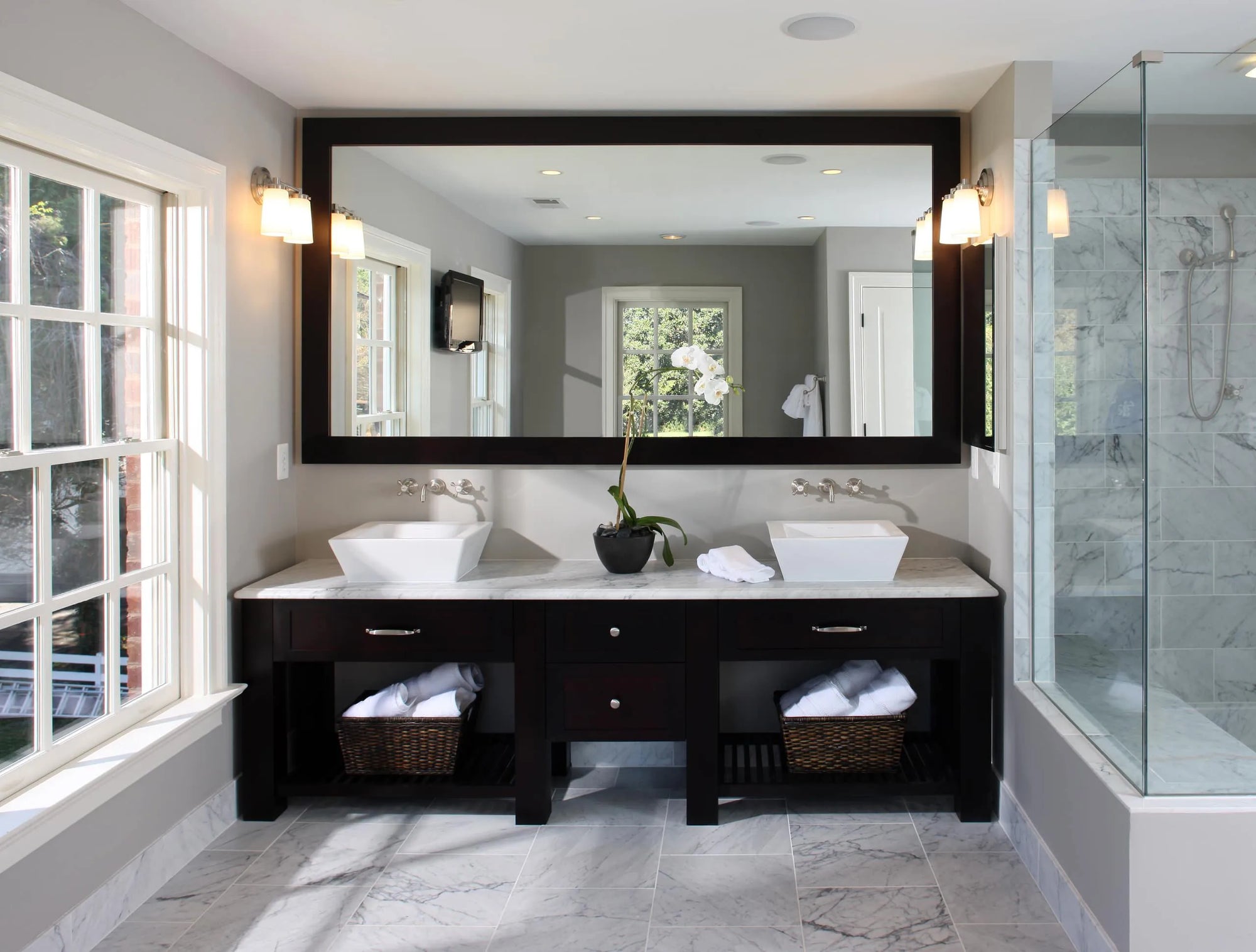 Double vanity with large framed mirror and glass shower in neutral bathroom.