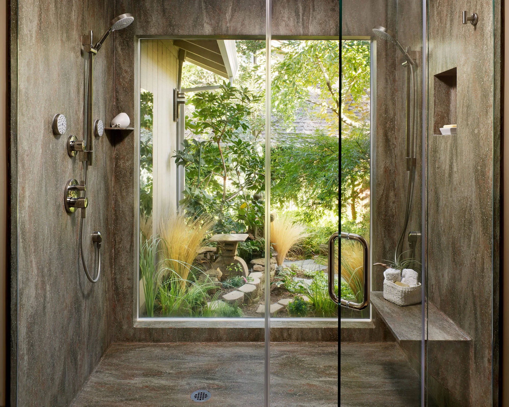 Luxury full body shower system with glass walls, bench, and garden view in a modern indoor-outdoor bathroom design.