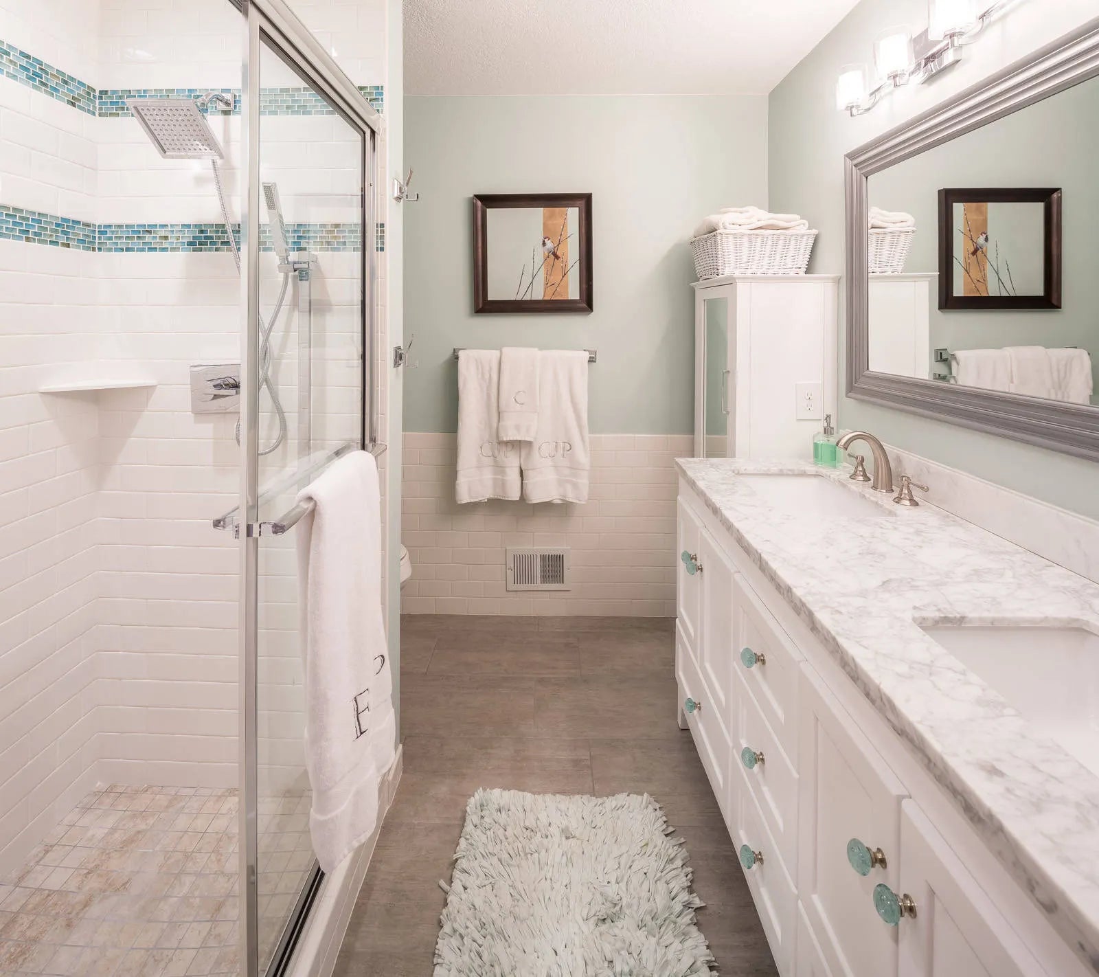 Sleek bathroom featuring framed glass shower door, double vanity, mint walls & mosaic tiles.