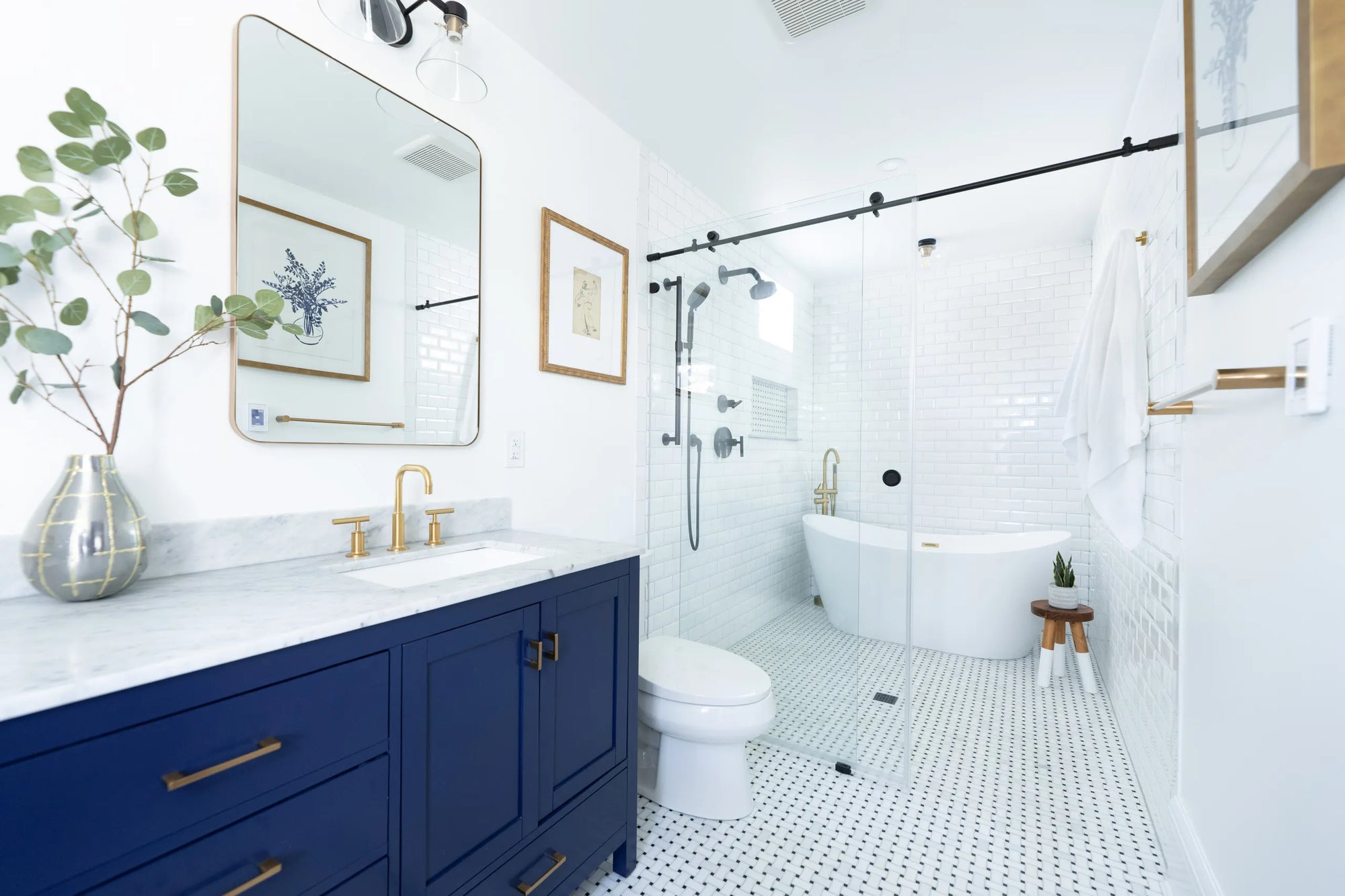 Modern bathroom with frameless sliding shower door, freestanding tub, navy vanity, gold fixtures, and white tiles.