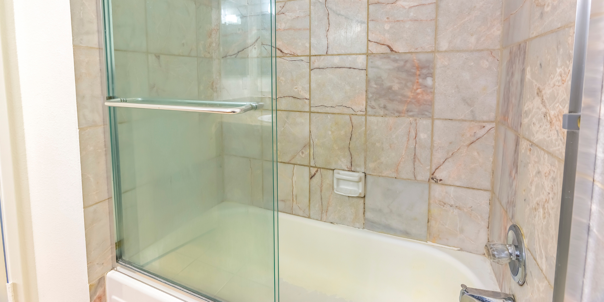 Bathtub glass door with frosted sliding panels, installed in a classic bathroom with marble-patterned tiles