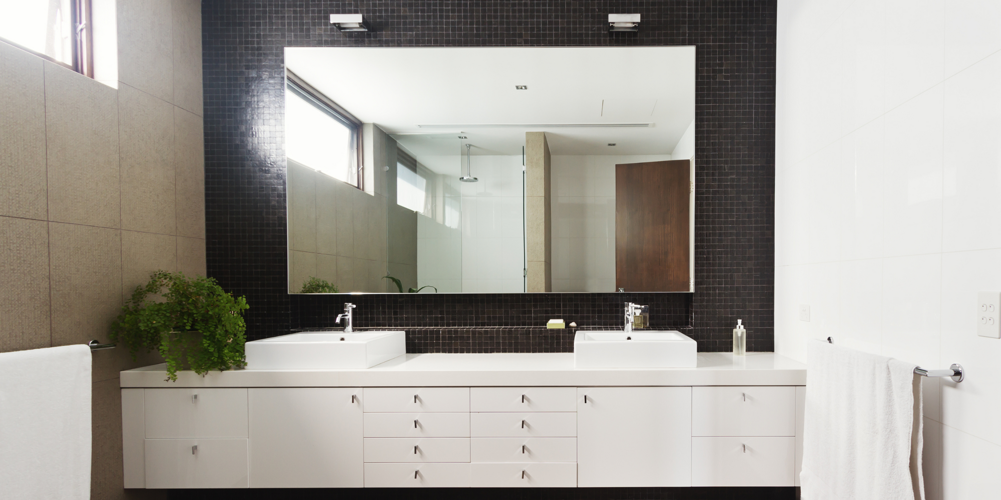 Modern bathroom vanities with mirror, double sinks, white cabinetry, black mosaic backsplash, and minimalist design.