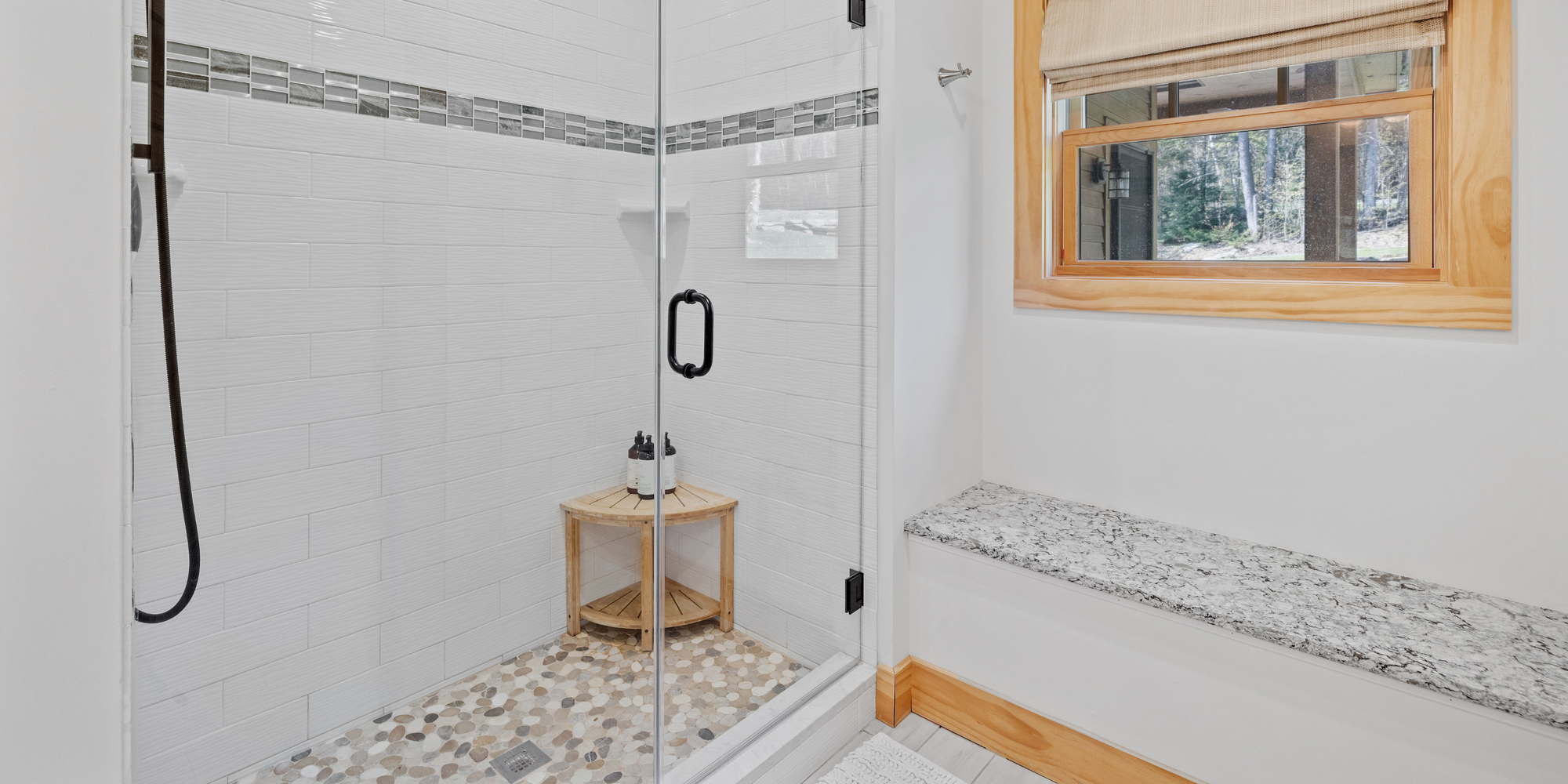 Tiled shower base with pebble flooring, glass enclosure, and modern white subway tile walls.