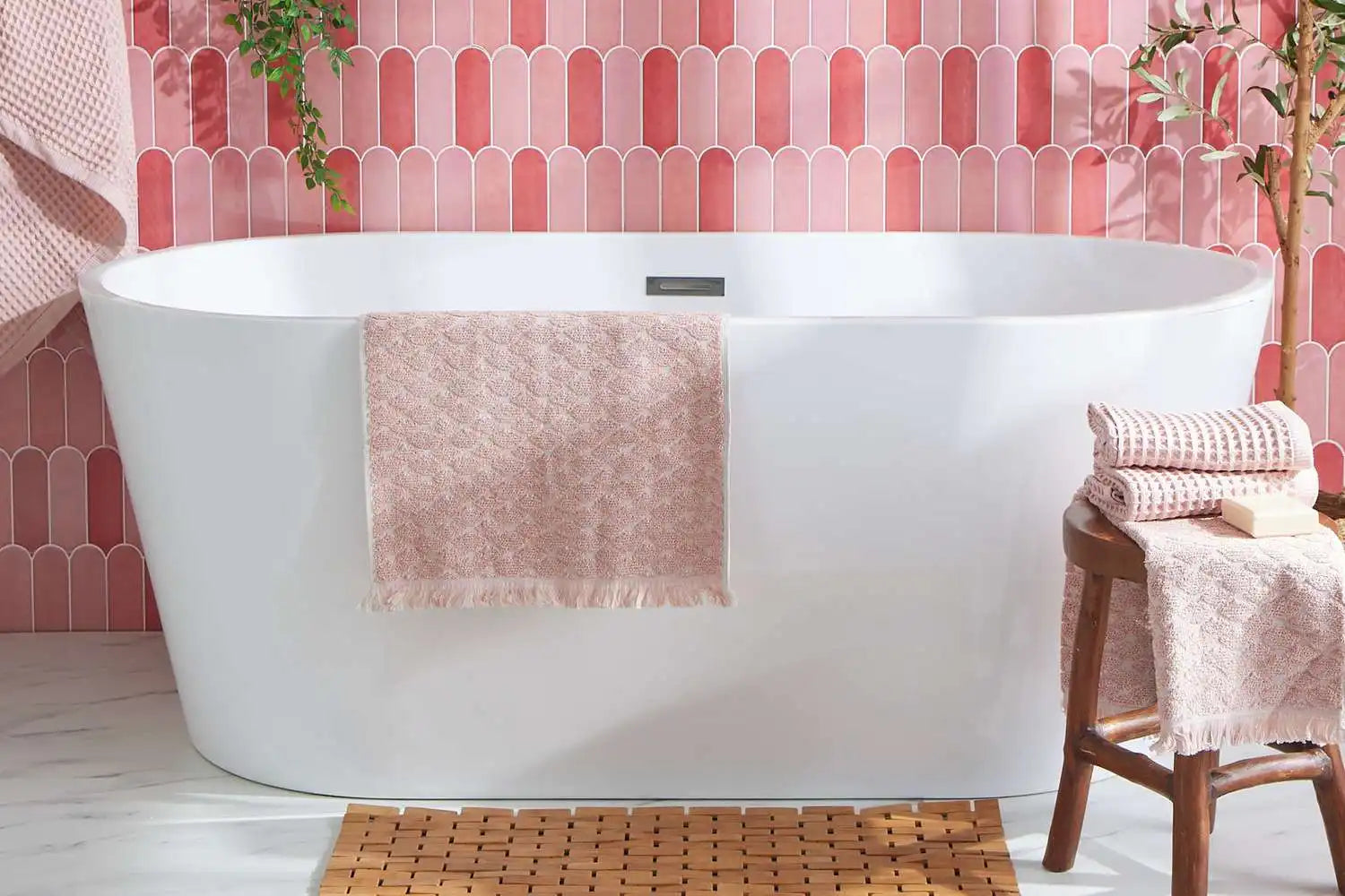 Freestanding soaking bathtub in a pink tile bathroom — a stylish example to consider when asking how many gallons does a bathtub hold.