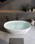 Matte white Abyss Series curved soaking tub filled with water in an elegant bathroom.