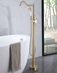 Brushed gold freestanding tub faucet with handheld shower installed beside modern freestanding bathtub.