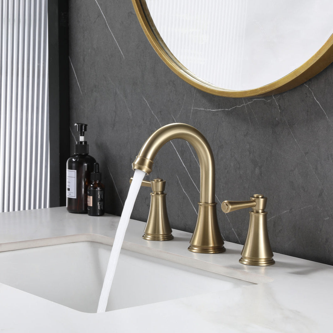 VALMIRA brushed gold sink faucet on white countertop with dark textured wall and gold mirror in background.