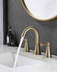 VALMIRA brushed gold sink faucet on white countertop with dark textured wall and gold mirror in background.