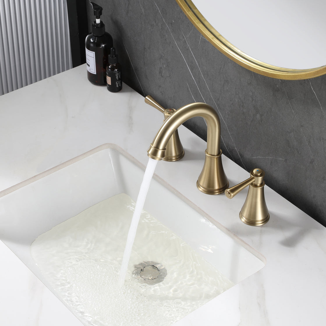 VALMIRA brushed gold sink faucet on white countertop with dark textured wall and gold mirror in background.