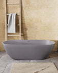 Nectar Series 63" freestanding tub showcasing its elegant oval silhouette, soft bath mat, and grey tile flooring.