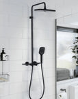 Matte black exposed thermostatic shower system with hand shower and tub spout in a white tiled bathroom.