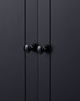 Close-up of matte black round knob on the door of tall storage cabinet.