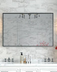 Noir Series mirror with beveled edge and metal frame installed in an elegant bathroom, flanked by sconces above a marble double vanity.