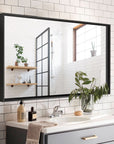 Noir Series black rectangular beveled-edge mirror installed in a modern minimalist bathroom, reflecting white tiles, wood accents, and greenery.