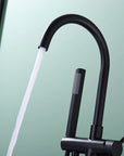 Close-up of Freestanding Black Tub Faucet with Handheld Shower, water stream flowing from spout.