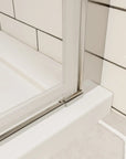 Chrome bottom track and seal detail on framed shower door over white shower base | Ace Decor