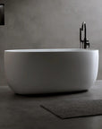 Lissome 47-inch oval soaking bathtub with black freestanding faucet and bath products, on dark grey minimalist background.