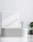 Nectar Series 67-inch white soaking tub with vertical ribbed texture, silver faucet, cactus plant, and artistic accents in modern minimalist bathroom.