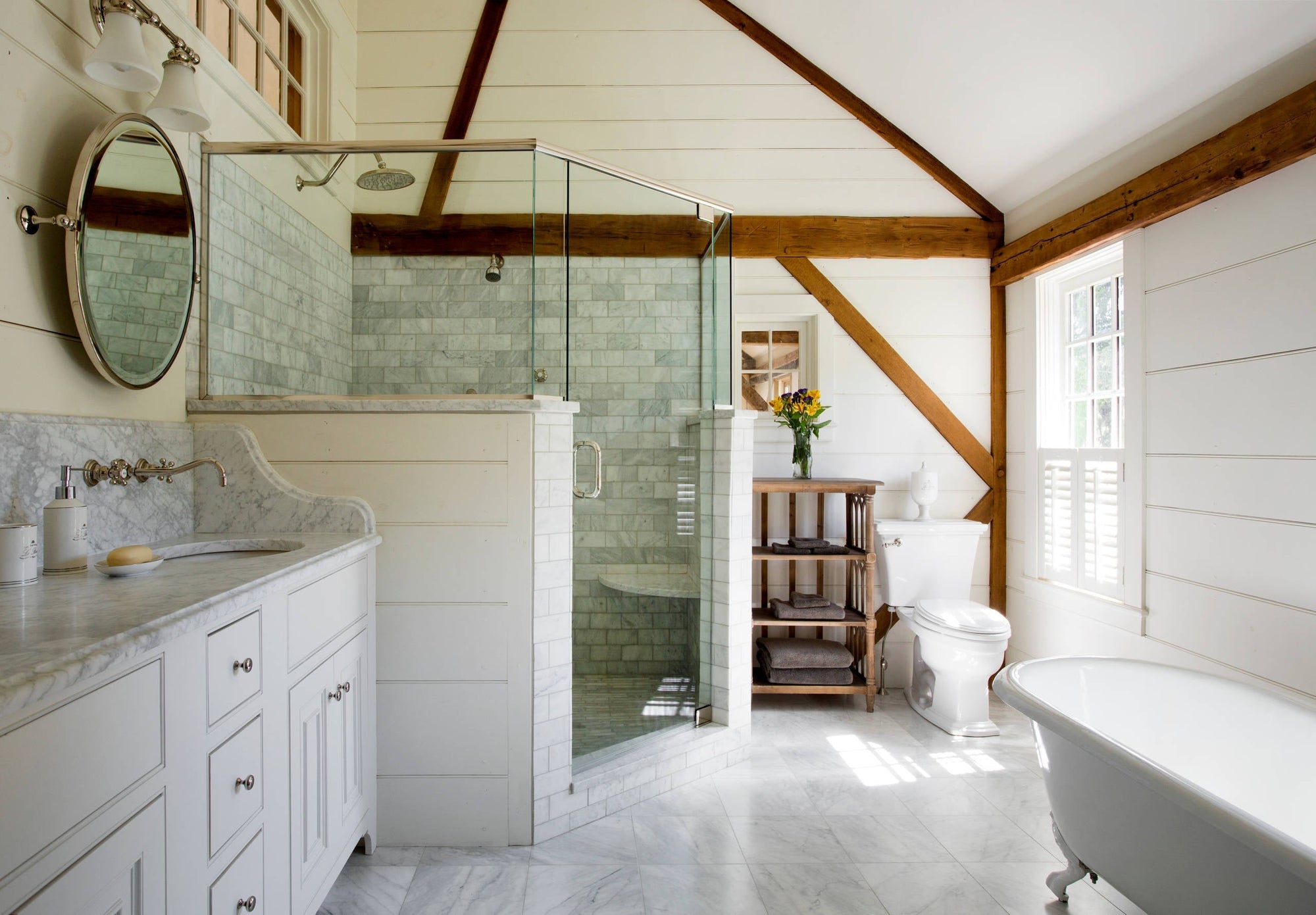 a bright, rustic bathroom with a marble vanity, a walk-in shower enclosed with glass, a freestanding bathtub, and a charming wooden shelf for storage. | ACE DECOR
