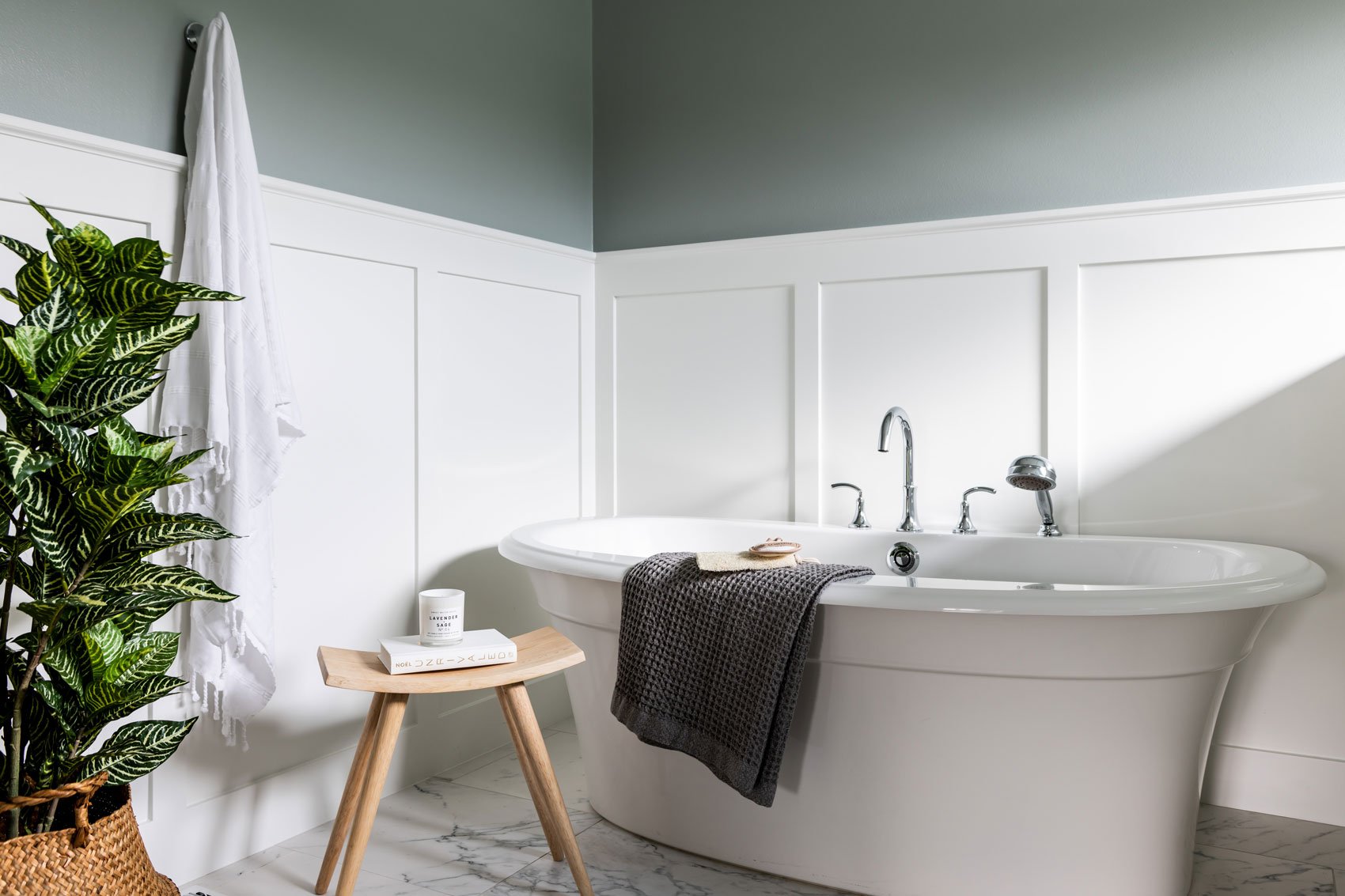 a stylish bathroom featuring a white freestanding soaking bathtub, elegant panel walls, a wooden stool with decor, and a cozy spa-like ambiance. | ACE DECOR