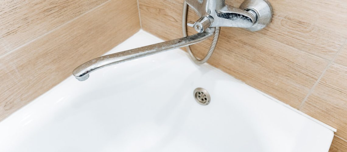 A close-up of a bathtub faucet with no visible bathtub overflow cover, showing the bathtub drain