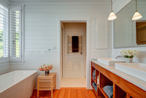 A bright, airy bathroom featuring a Heated Towel Bar Rack on the wall, complemented by wooden accents and a freestanding bathtub. | ACE DECOR
