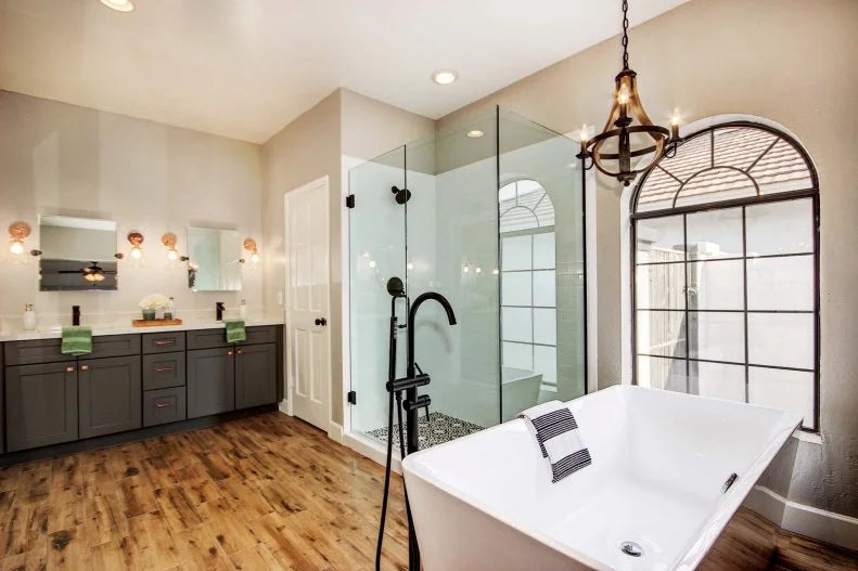 a spacious, elegant bathroom with wood flooring, a freestanding tub, and sleek Frameless Hinged Shower Doors enclosing a large glass shower area. | ACE DECOR
