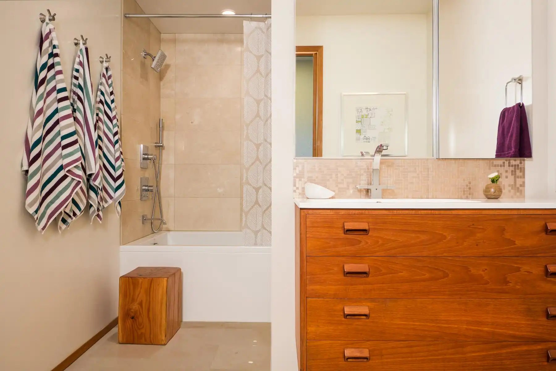 A modern bathroom with wooden accents, striped towels, and small bathtubs paired with a shower and beige tiles. |ACE DECOR