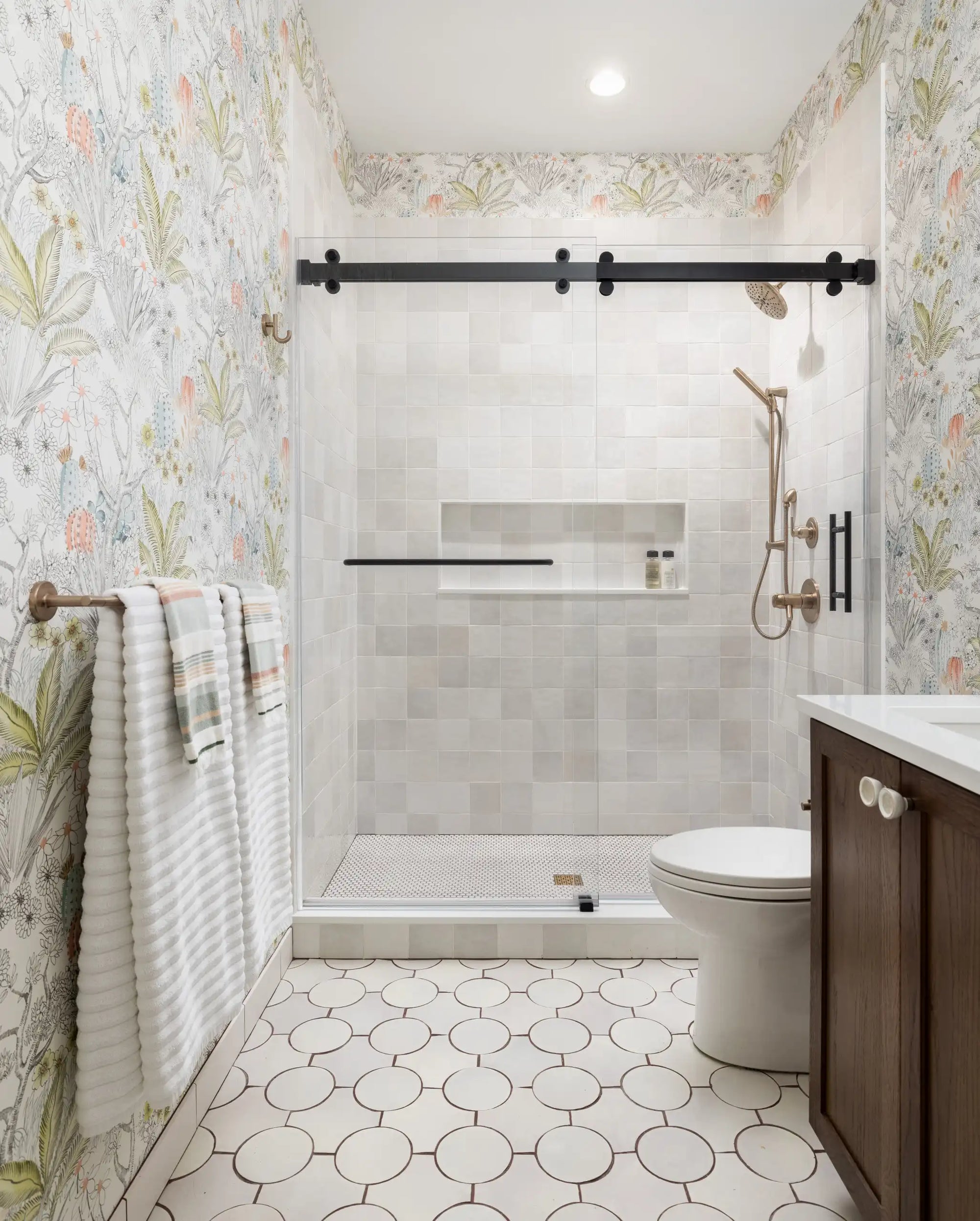 A bright, modern bathroom featuring elegant bathroom sliding glass shower doors with matte black hardware and botanical wallpaper accents. | ACE DECOR