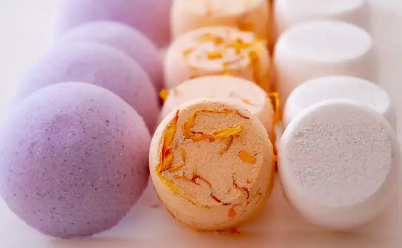 Colorful handmade shower steamers in purple, orange, and white tones arranged neatly for a spa-inspired display | ACE DECOR