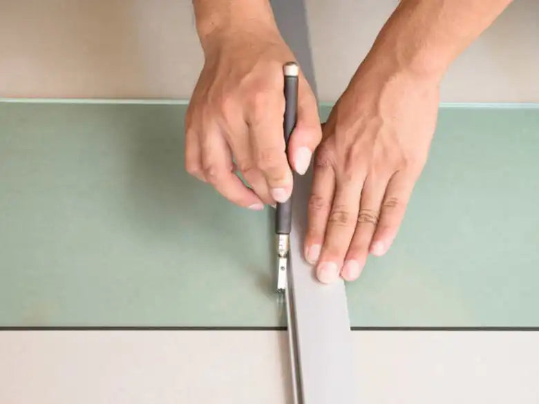 Person scoring glass sheet with a cutter tool to demonstrate how to cut tempered glass safely | Ace Decor