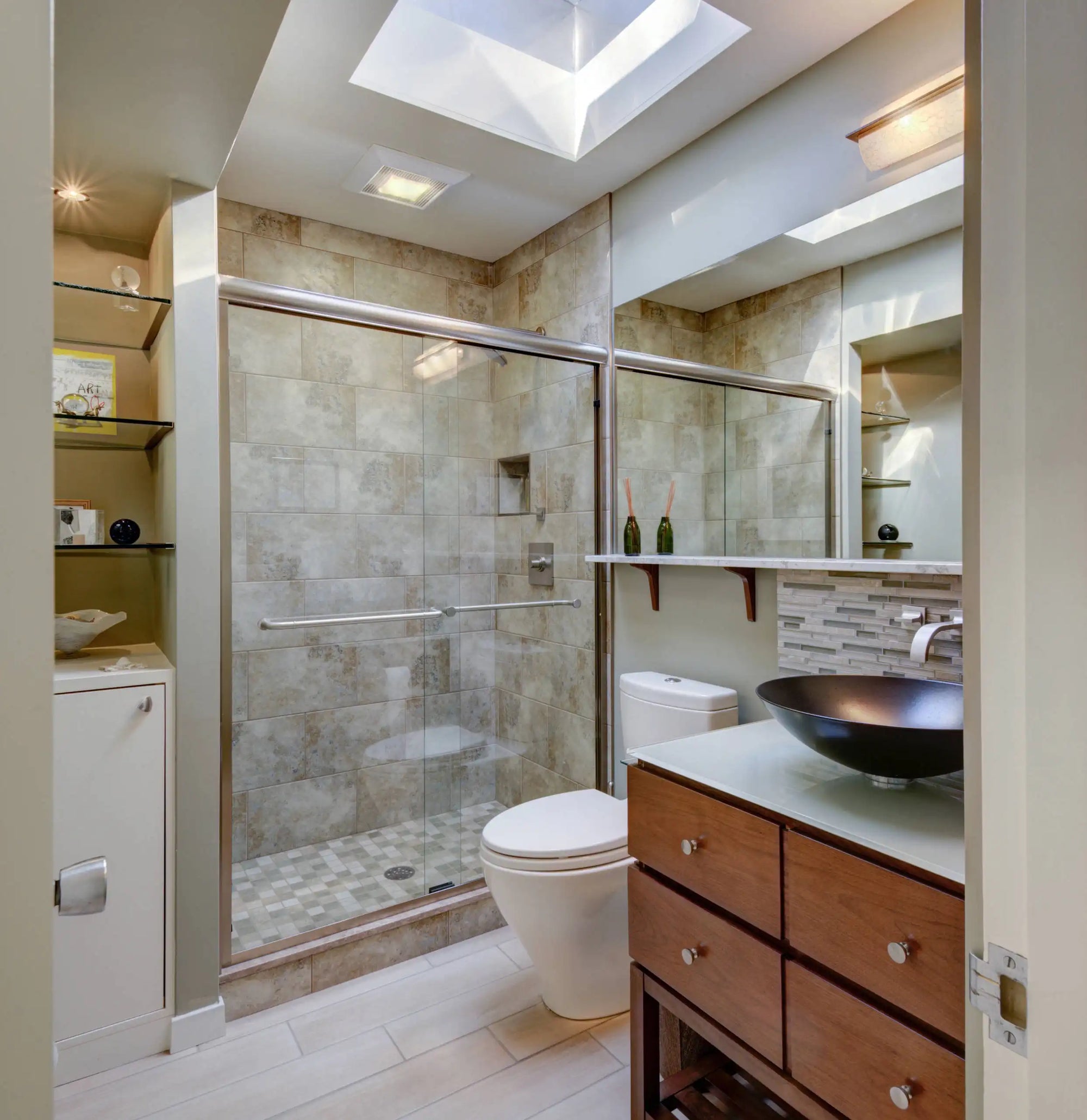 A modern bathroom with beige tiles features glass shower doors sliding next to a sleek vanity and skylight ceiling. |ACE DECOR