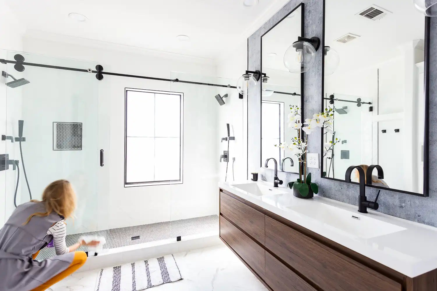 A modern bathroom featuring a large glass shower enclosure with matte black hardware and a double vanity with wood cabinets. | ACE DECOR