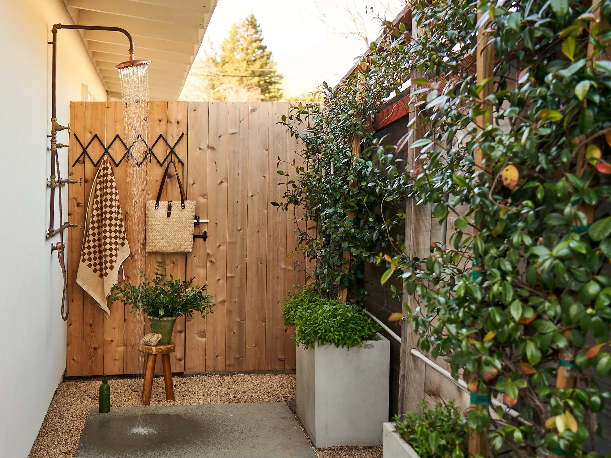 a stylish DIY outdoor shower with a wooden enclosure, plants, and accessories like towels and a stool. | ACE DECOR