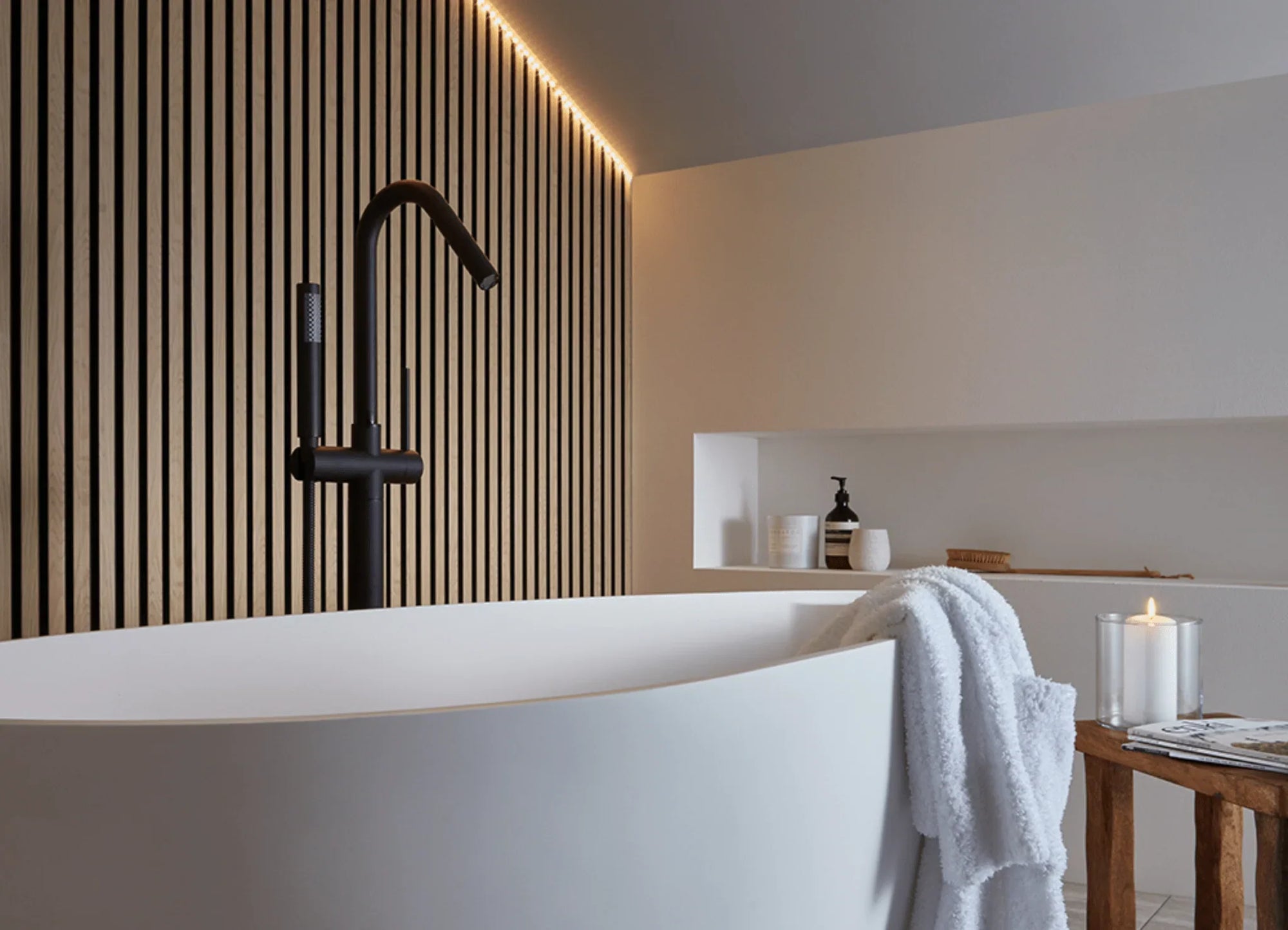 a freestanding bathtub in the middle of slatted wood paneled walls with lots of soft light and a minimalist entryway to the bathroom. | ACE DECOR