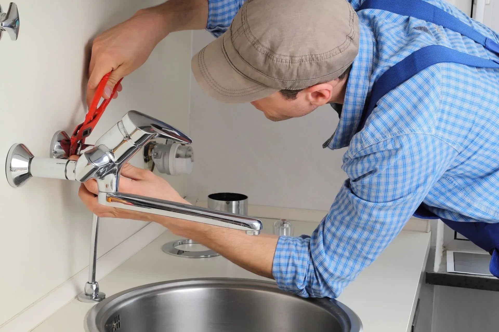 Plumber performing bathroom faucet repair using a wrench on a wall-mounted chrome fixture above a sink | Ace Decor