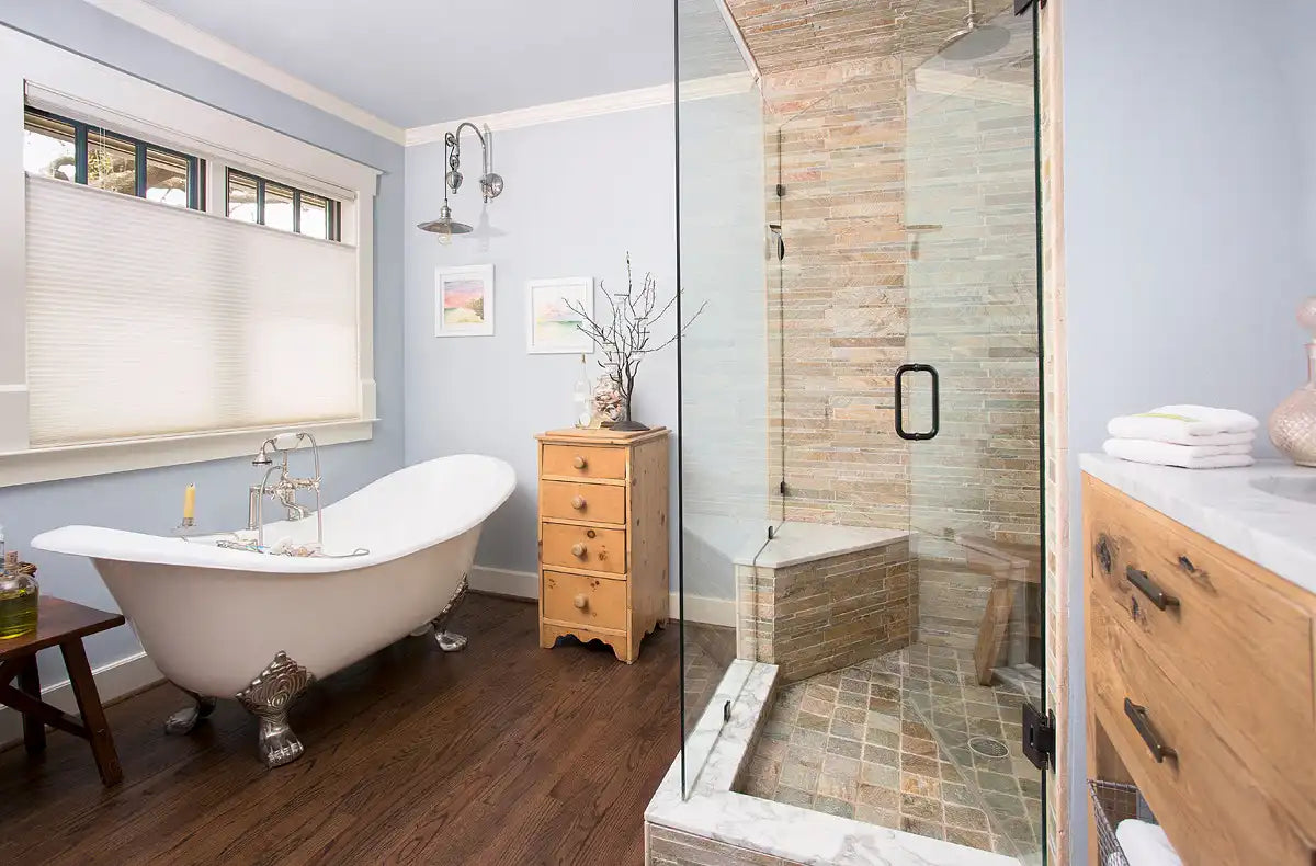 This bathroom features a frameless hinged glass shower enclosure with stone tile walls, showcasing one of the elegant types of shower doors. | ACE DECOR