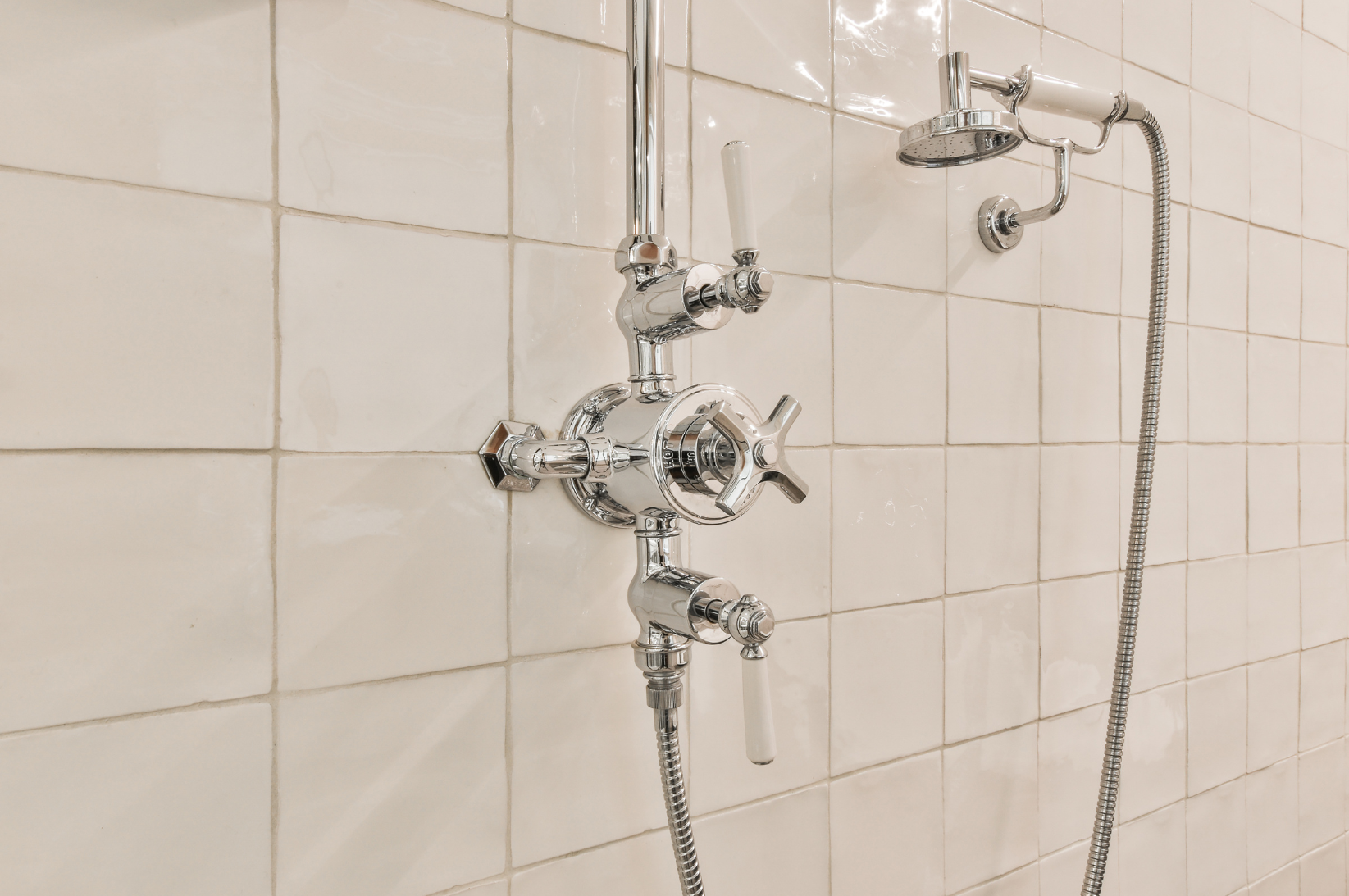 A close-up of a vintage-style shower control with chrome fittings and white tile background.