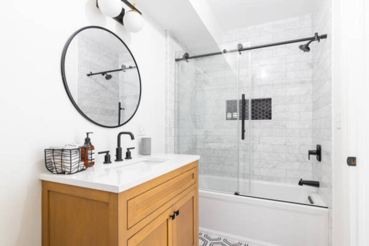 A modern bathroom featuring a bathtub glass door, wood vanity, and black fixtures. | ACE DECOR