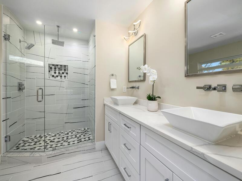 a modern bathroom featuring frameless shower doors, a double vanity with vessel sinks, and sleek white cabinetry. | ACE DECOR