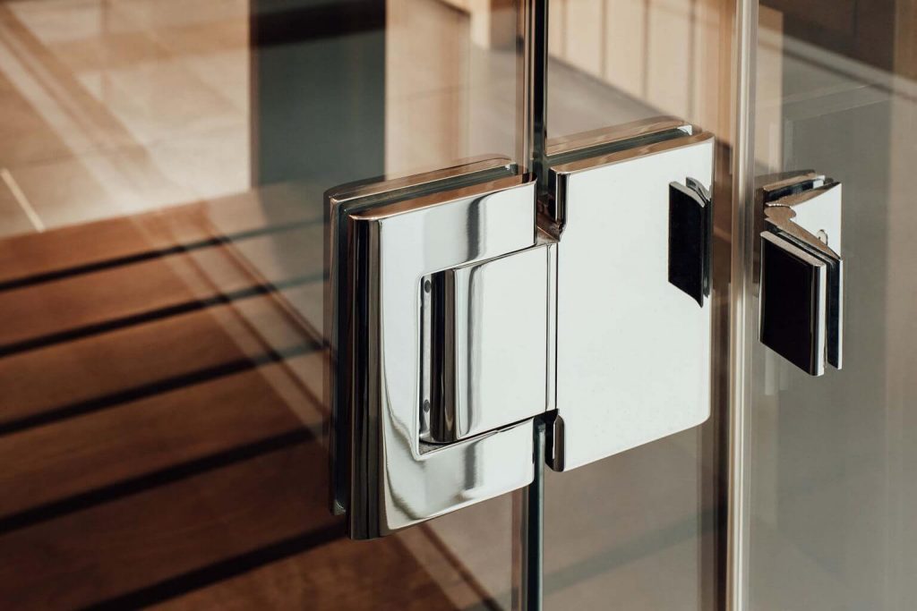 Close-up of a frameless shower door hinge with a sleek, modern chrome finish. | ACE DECOR