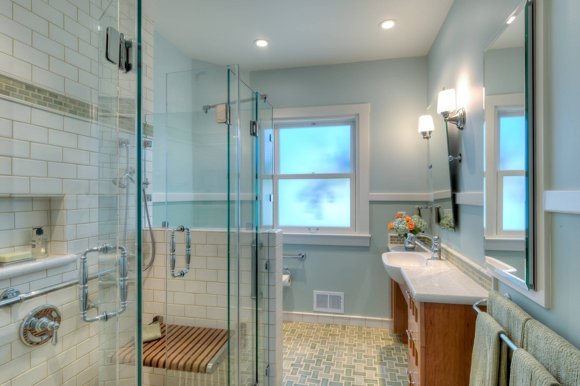 A bright, accessible bathroom featuring a glass bi-fold shower door, built-in bench, and modern vanity setup | ACE DECOR